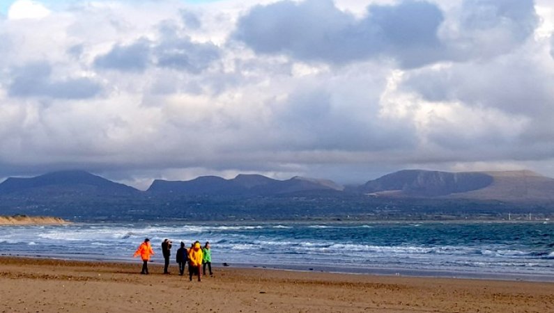 Members of the Urban Saints Impact Team walking along the beach in Anglesey, with dramatic seas and sky behind them - during the Impact Team's time away together in October 2019